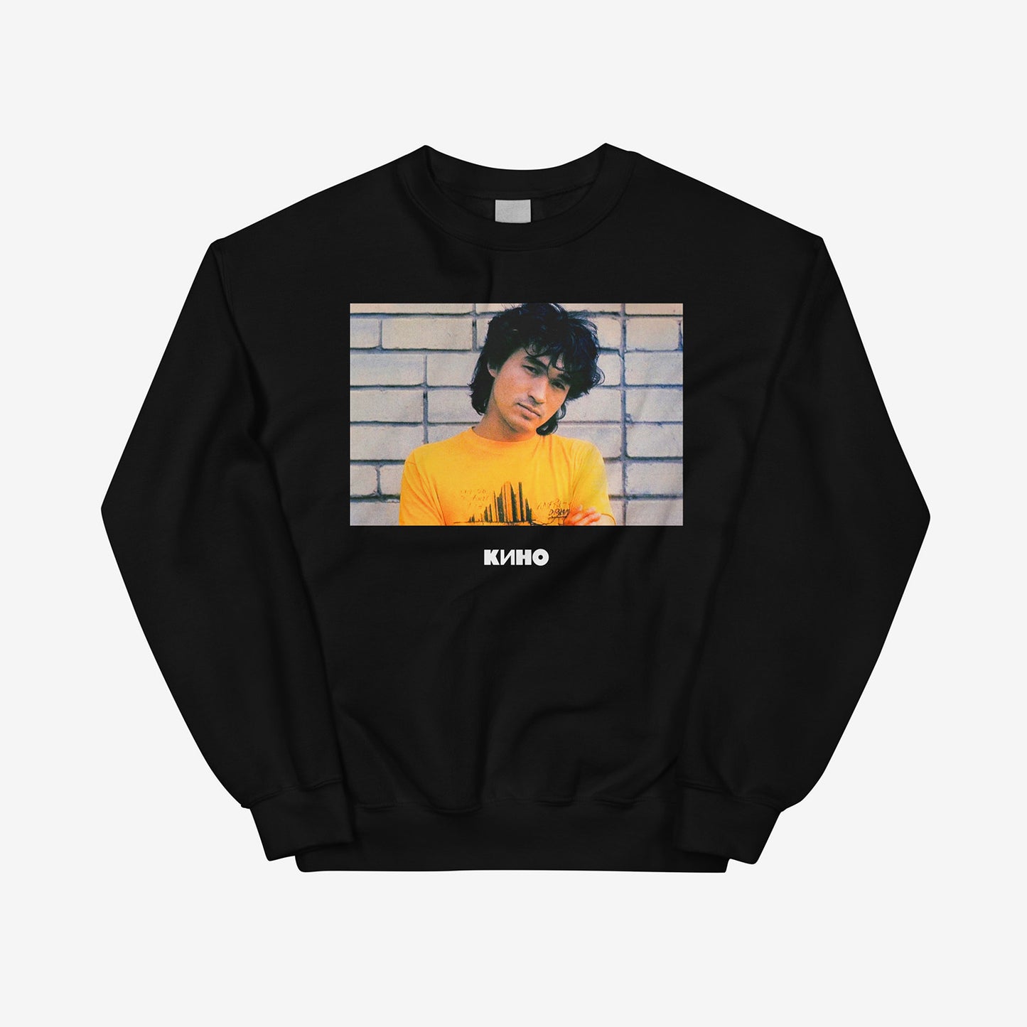 Rare archival photo of Viktor Tsoi in a yellow T-shirt against a white brick wall with a little KINO logo underneath, printed on the front of a heavyweight black unisex sweatshirt with a KINO logo on the back neck side, from GruppaKino.com. Front side.