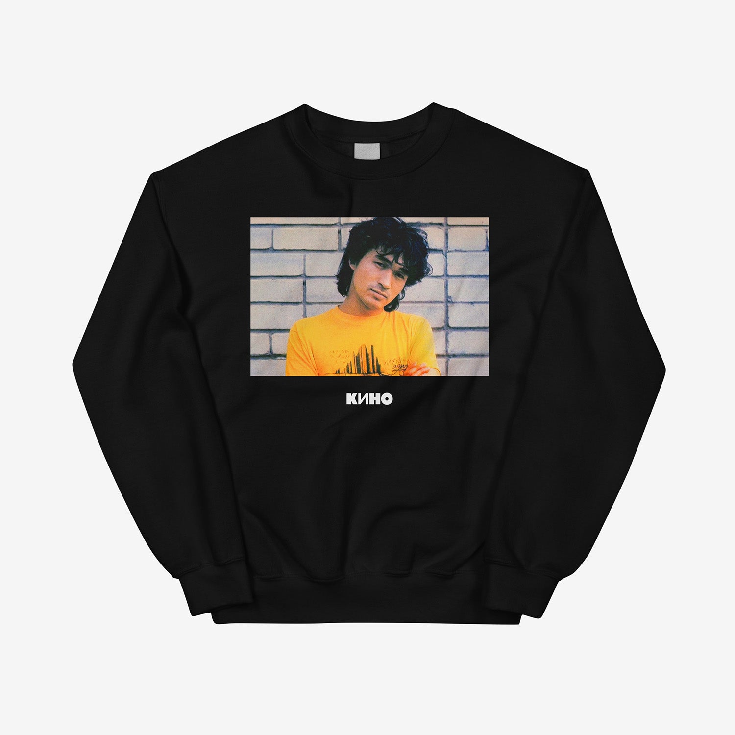Rare archival photo of Viktor Tsoi in a yellow T-shirt against a white brick wall with a little KINO logo underneath, printed on the front of a heavyweight black unisex sweatshirt with a KINO logo on the back neck side, from GruppaKino.com. Front side.